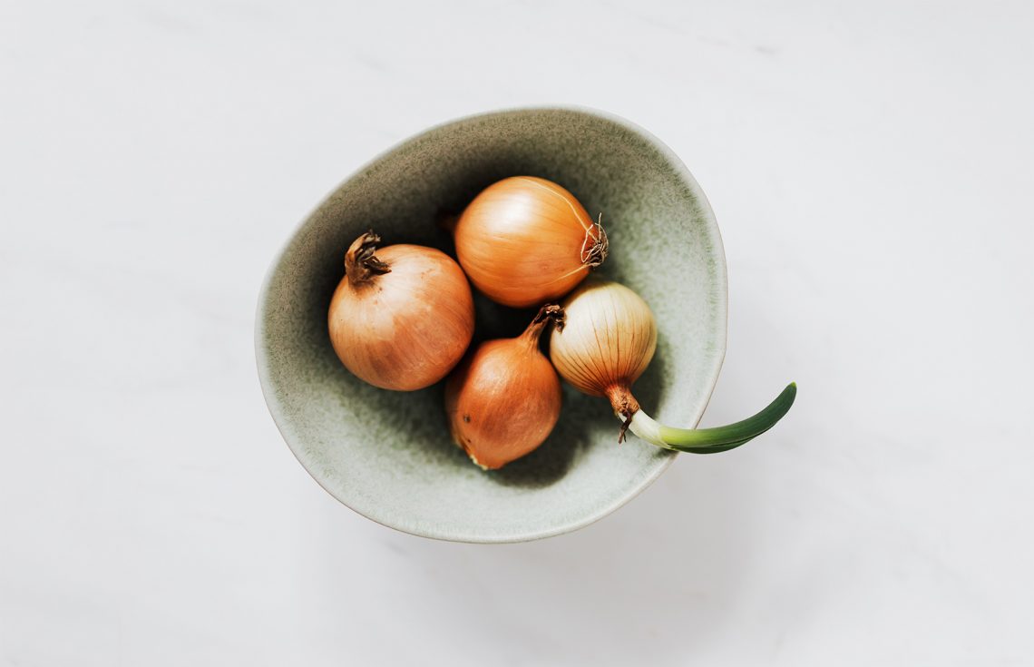 Tekst o zdrowotnych właściwościach domowego syropu z cebuli. Na zdjęciu: Miska cebuli i kiełek - HelloZdrowie