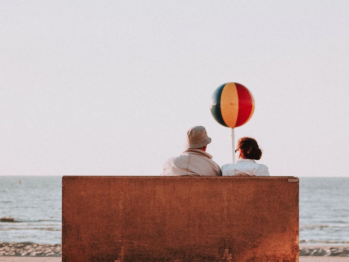 Tekst o starzeniu się mózgu i jego aspektach. Na zdjęciu: Mężczyzna i kobieta siedzący na ławce z piłką plażową - HelloZdrowie