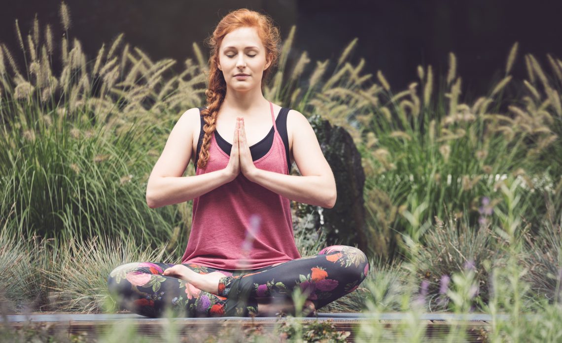 Tekst o prostych wskazówkach do medytacji na weekend. Na zdjęciu: Kobieta medytująca na trawie - HelloZdrowie