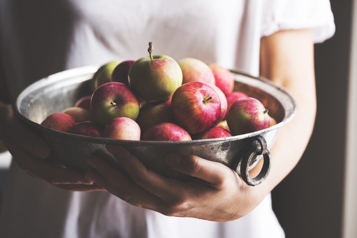 Tekst o nadziewanych pieczonych jabłkach i ich wartościach. Na zdjęciu: Osoba trzymająca miseczkę jabłek - HelloZdrowie
