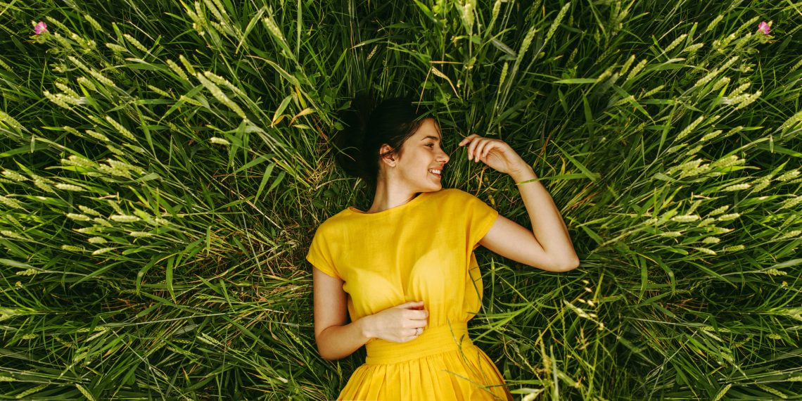 Tekst o zaletach niepokalanka pospolitego w łagodzeniu PMS. Na zdjęciu: Kobieta leżąca na trawie - HelloZdrowie