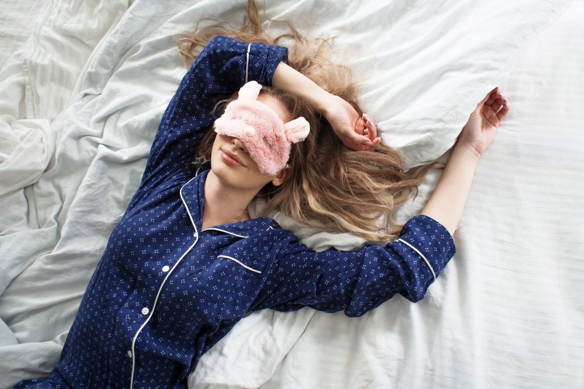 Tekst o najzdrowszej pozycji do spania. Na zdjęciu: Kobieta leżąca na łóżku z maską na oczach - HelloZdrowie