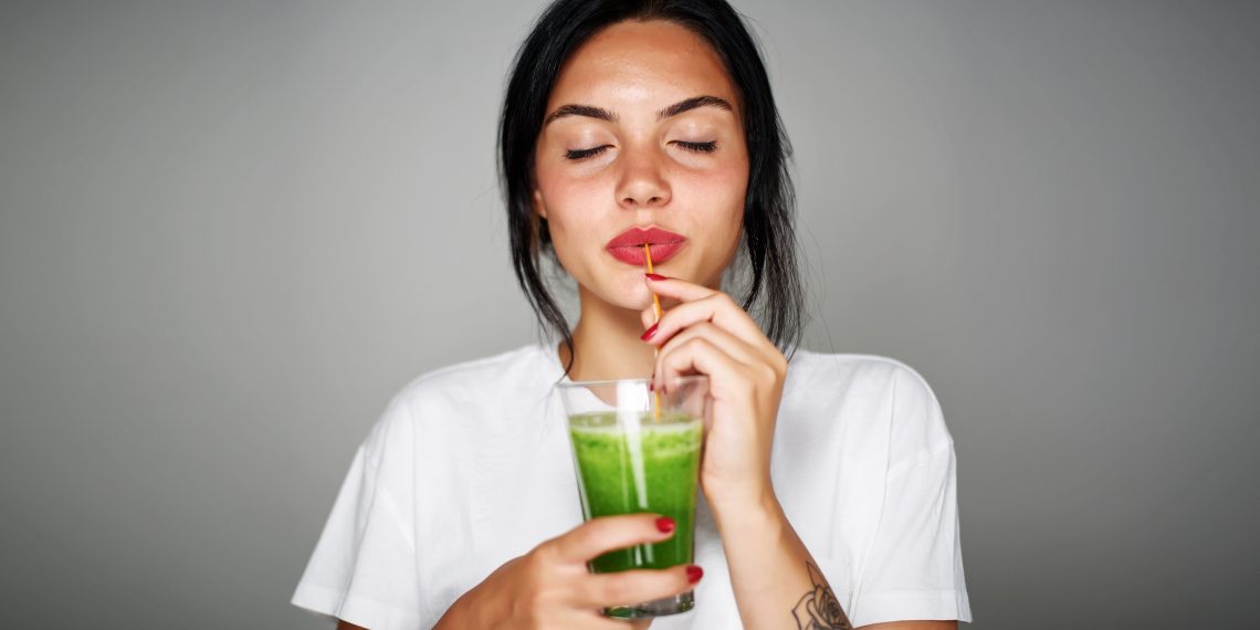 Tekst o wegańskich sposobach na kaca po imprezie. Na zdjęciu: Kobieta pijąca zielony koktajl - HelloZdrowie