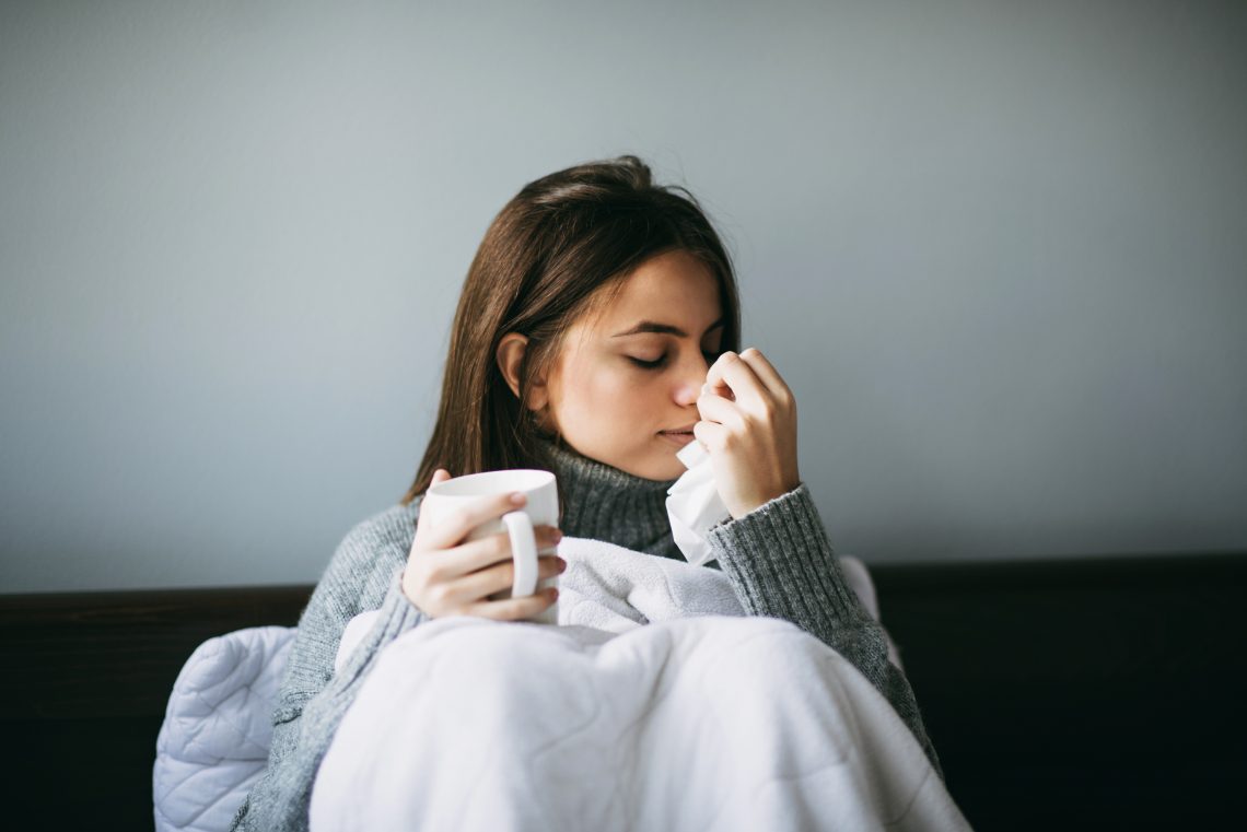 Tekst o długości zarażania podczas przeziębienia. Na zdjęciu: Kobieta trzymająca chusteczkę i kubek - HelloZdrowie