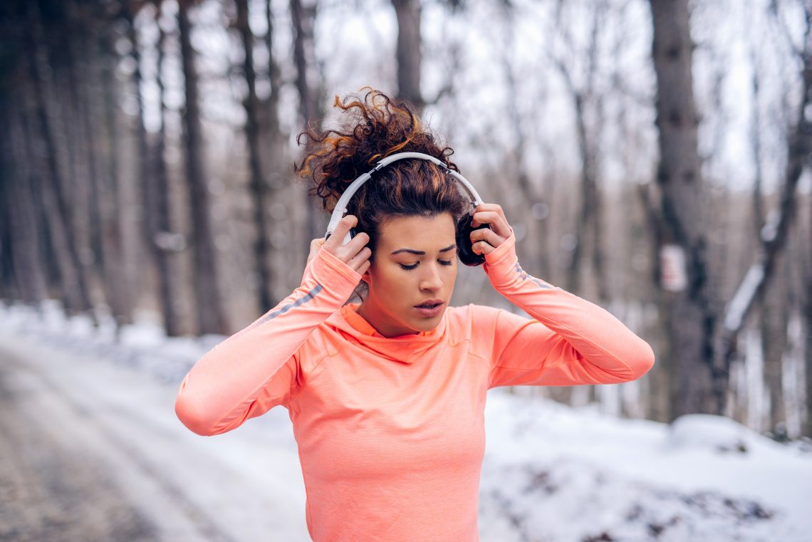 Tekst o zasadach bezpiecznego biegania zimą. Na zdjęciu: Kobieta nosząca słuchawki i trzymająca się za głowę - HelloZdrowie