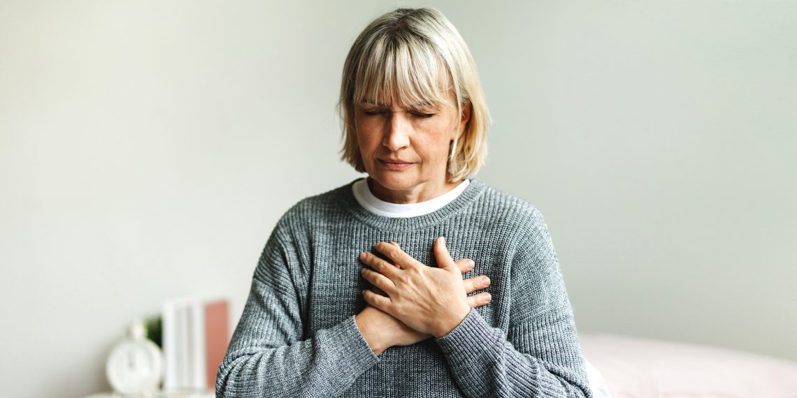 Tekst o mniej oczywistych objawach zawału serca. Na zdjęciu: Kobieta trzymająca się za klatkę piersiową - HelloZdrowie