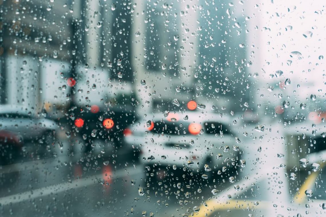 Tekst o przyczynach przeziębień podczas zmiany pogody. Na zdjęciu: Samochód jedzie ulicą przez krople deszczu na szybie - HelloZdrowie