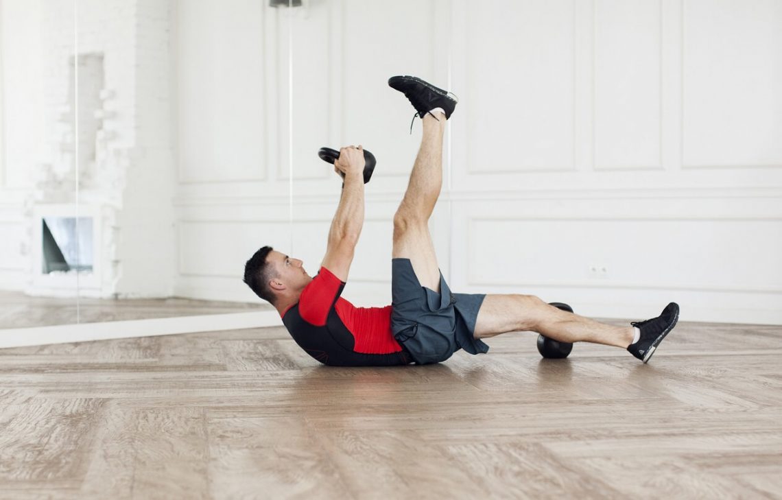 Tekst o treningu siłowym w domu z kettlebells. Na zdjęciu: Mężczyzna wykonujący ćwiczenie push-up z ciężarami - HelloZdrowie