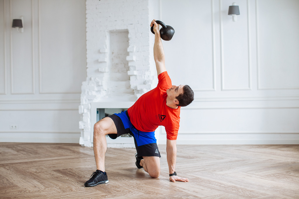 Tekst o metodach treningowych z kettlebells i ich różnicach. Na zdjęciu: Mężczyzna podnoszący kettlebell - HelloZdrowie