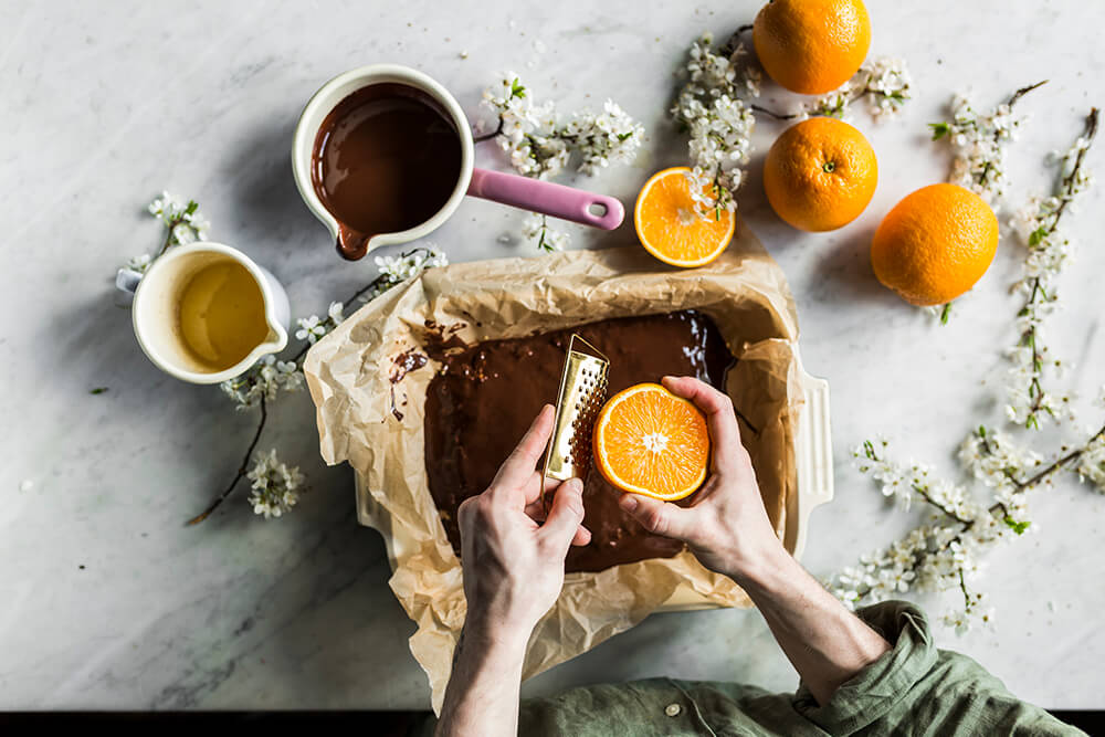 Tekst o zdrowym deserze z migdałami i czekoladą. Na zdjęciu: Osoba wyciskająca pomarańczę do brownie - HelloZdrowie