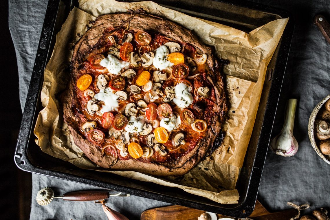 Tekst o zdrowej pizzy na spodzie z fasoli. Na zdjęciu: Pizza z pomidorami i grzybami na blasze do pieczenia - HelloZdrowie
