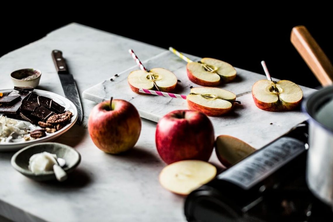 Tekst o smacznym i zdrowym deserze z jabłkami. Na zdjęciu: Jabłka pokrojone na plastry na marmurowej desce - HelloZdrowie