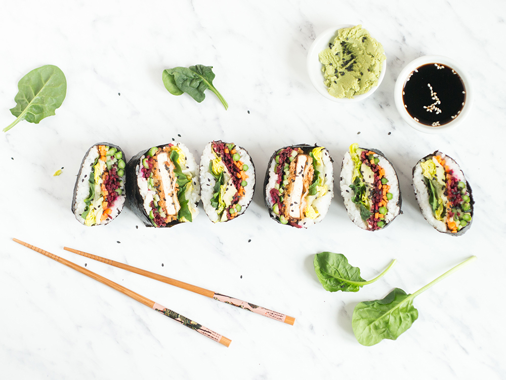 Tekst o przygotowaniu onigirazu ze szparagami na majówkę. Na zdjęciu: Rolki sushi ułożone w rzędzie z pałeczkami i sosami - HelloZdrowie
