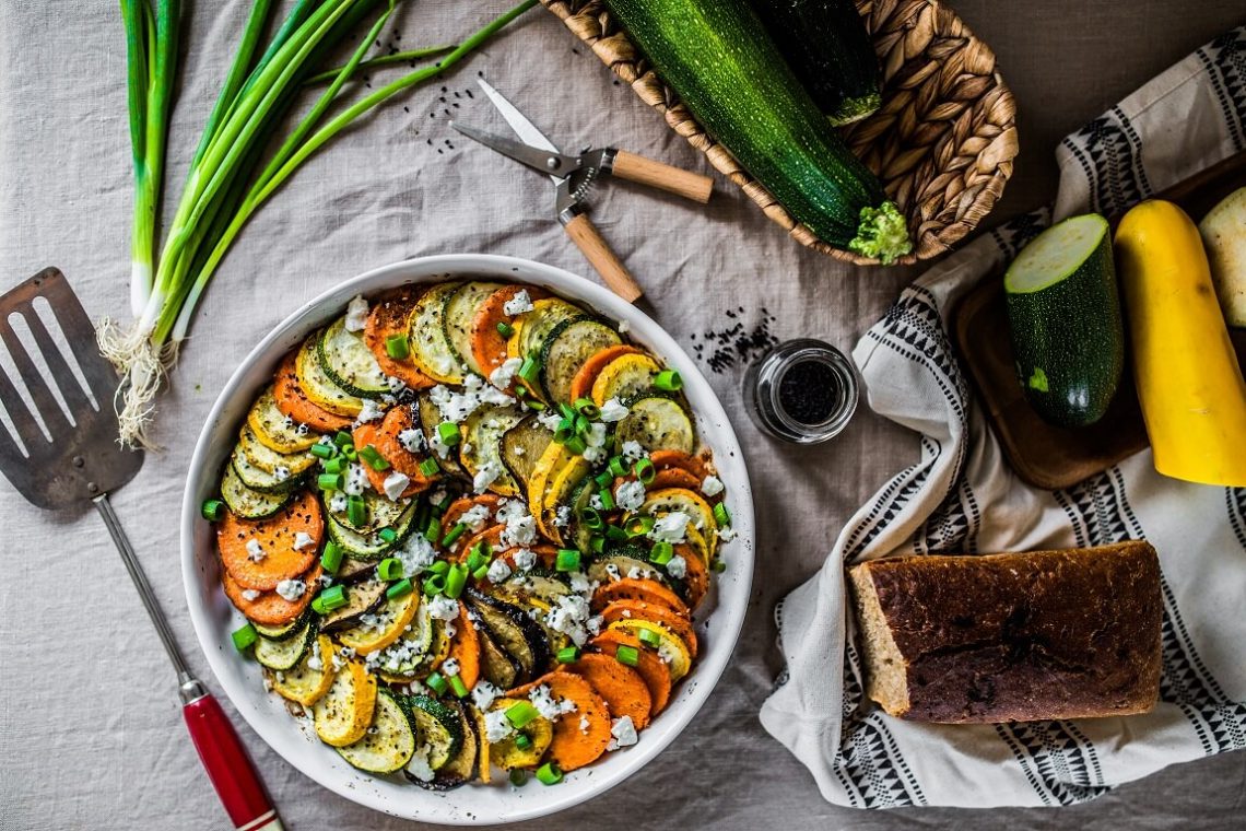 Tekst o przygotowaniu tianu, letniej potrawy warzywnej. Na zdjęciu: Miska jedzenia obok kosza warzyw - HelloZdrowie