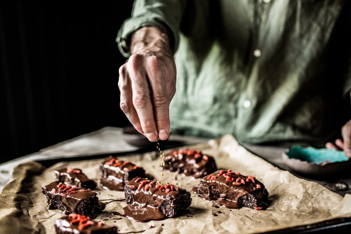 Tekst o zdrowym brownie z dodatkiem superfoods. Na zdjęciu: Osoba nalewająca czekoladę na blachę z brownies - HelloZdrowie