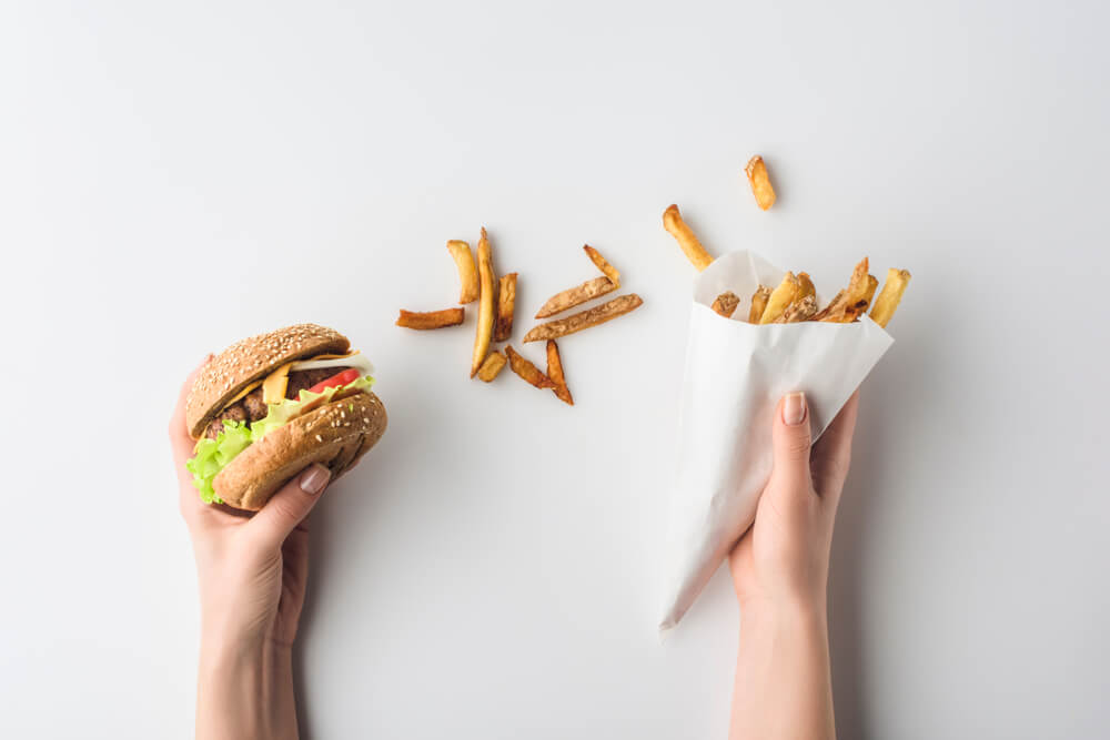 Tekst o wpływie fast foodu na układ odpornościowy. Na zdjęciu: Osoba trzymająca hamburgera i frytki - HelloZdrowie