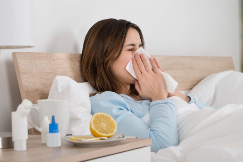 Przeziębiona kobieta leży w łóżku i leczy się domowymi sposobami
