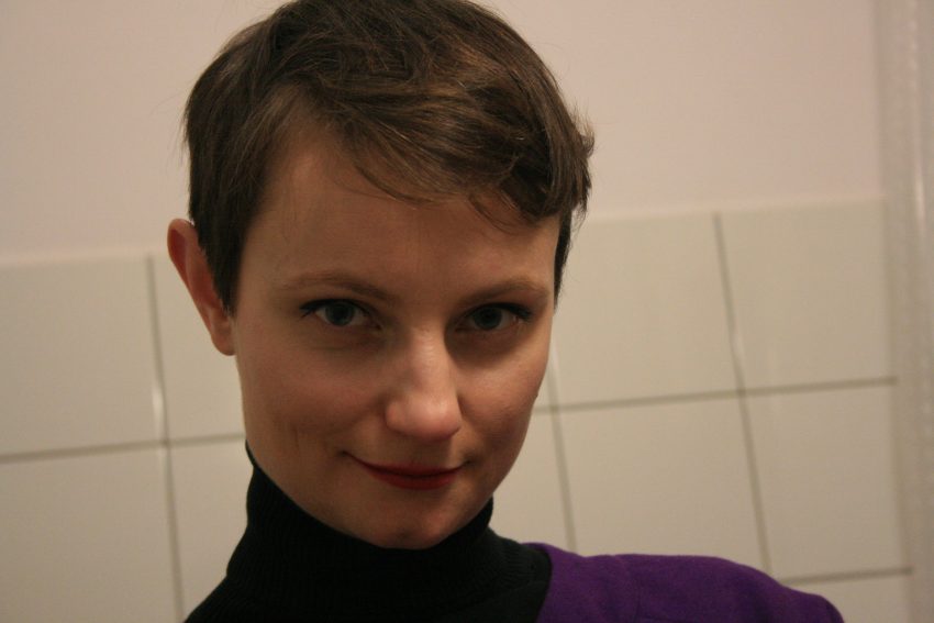 Tekst o kobietach walczących z rakiem piersi. Na zdjęciu: Kobieta z krótkimi włosami, ubrana w fioletowy sweter - HelloZdrowie