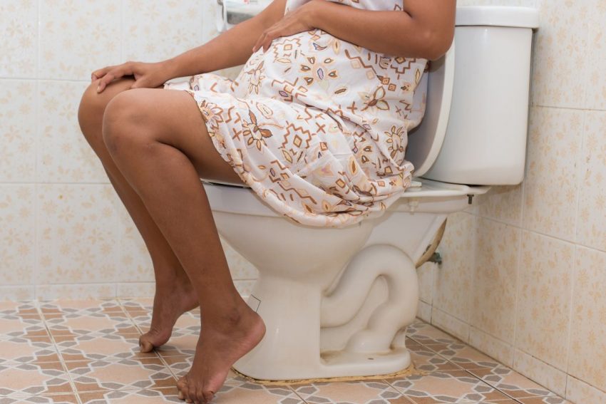 Kobieta w ciąży siedzi w łazience z powodu hemoroidów