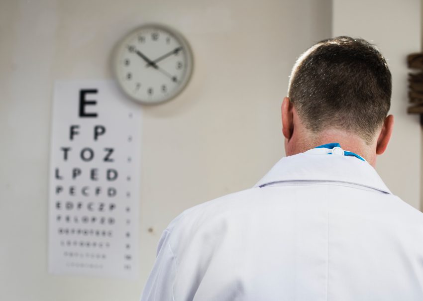 doktor stoi tyłem, na ścianieprzednimwisi zegar i tablica do sprawdzania wzroku