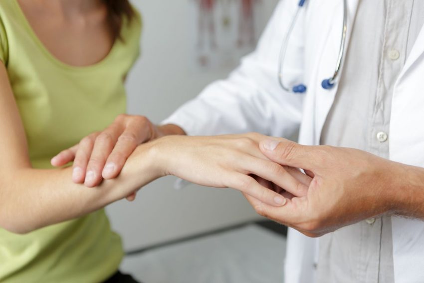 Lekarka trzyma dłoń pacjentki z zespołem cieśni nadgarstka