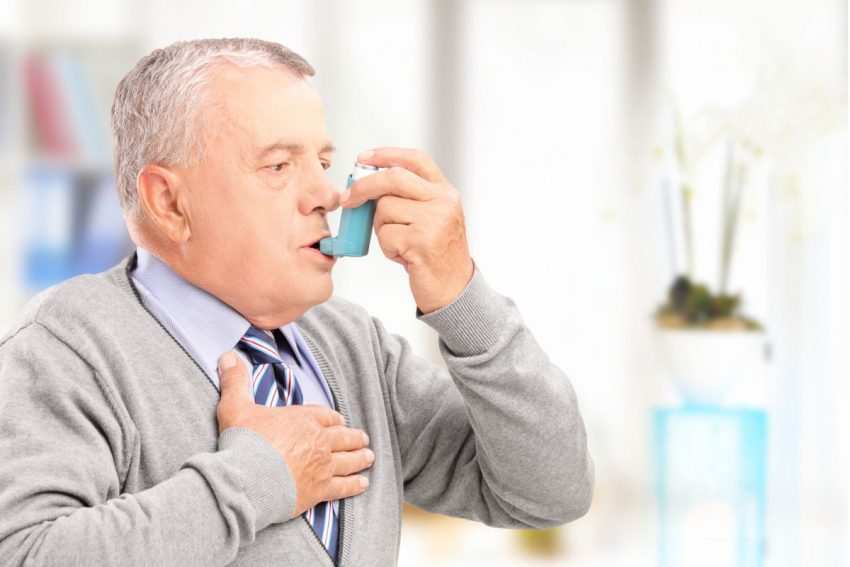 Mężczyzna z astmą sercową trzyma się za serce i bierze leki
