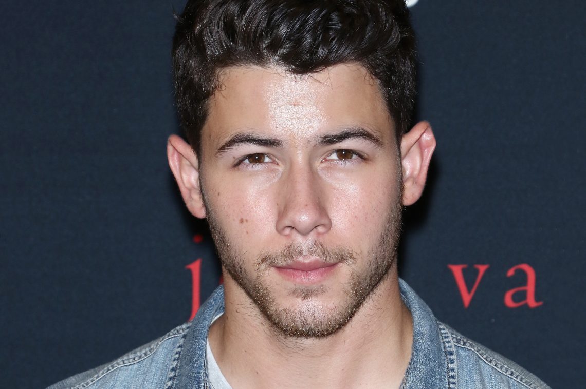 Piosenkarz, Nick Jonas pozuje na ciemnym tle. Zdjęcie do ramion.