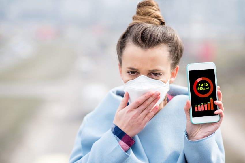 Kobieta w masce pokazuje na telefonie poziom stężenia pyłu smogowego