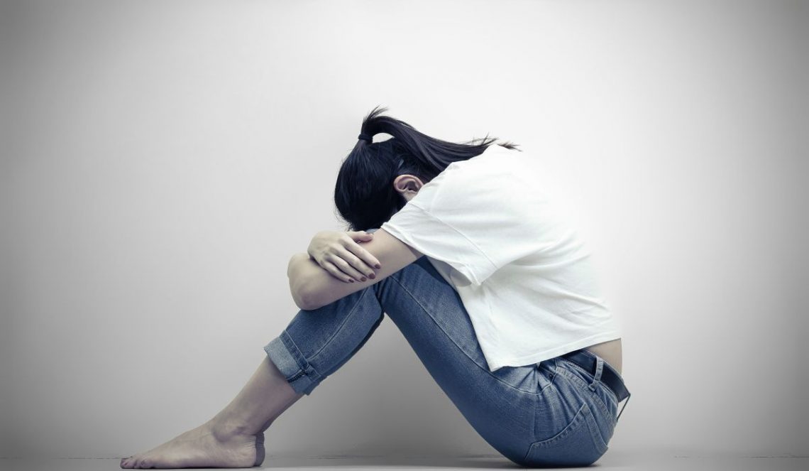 Smutna kobieta z depresją siedzi obejmując swoje kolana i płacząc