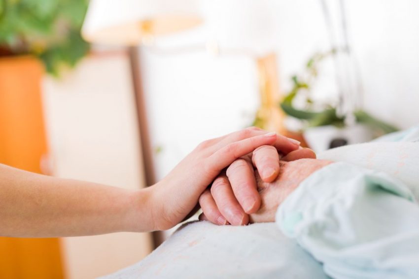 Osoba odwiedzająca osobę chorą na Parkinsona trzyma dłoń na jej dłoniach