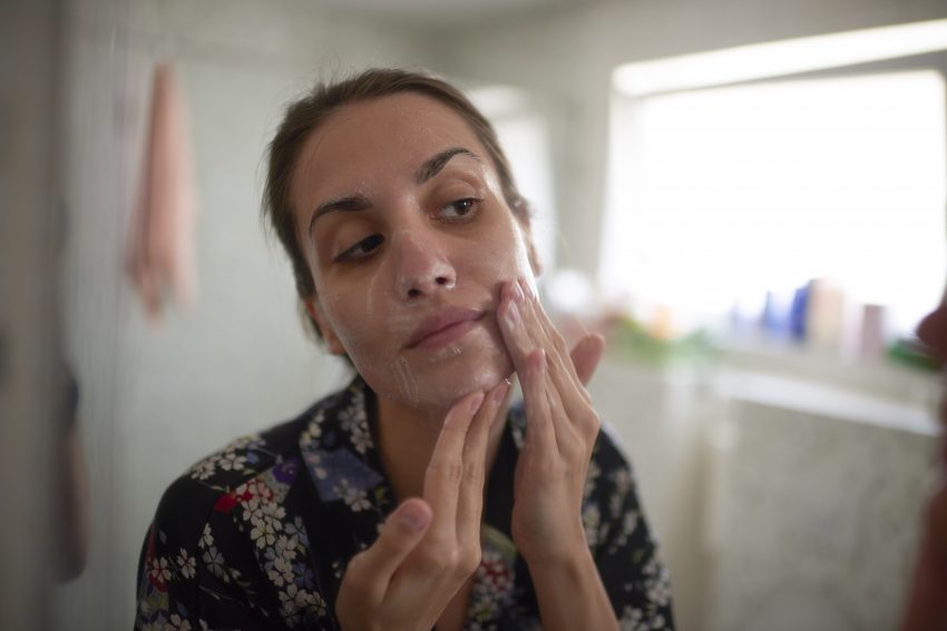 Kobieta smarująca twarz kremem w łazience