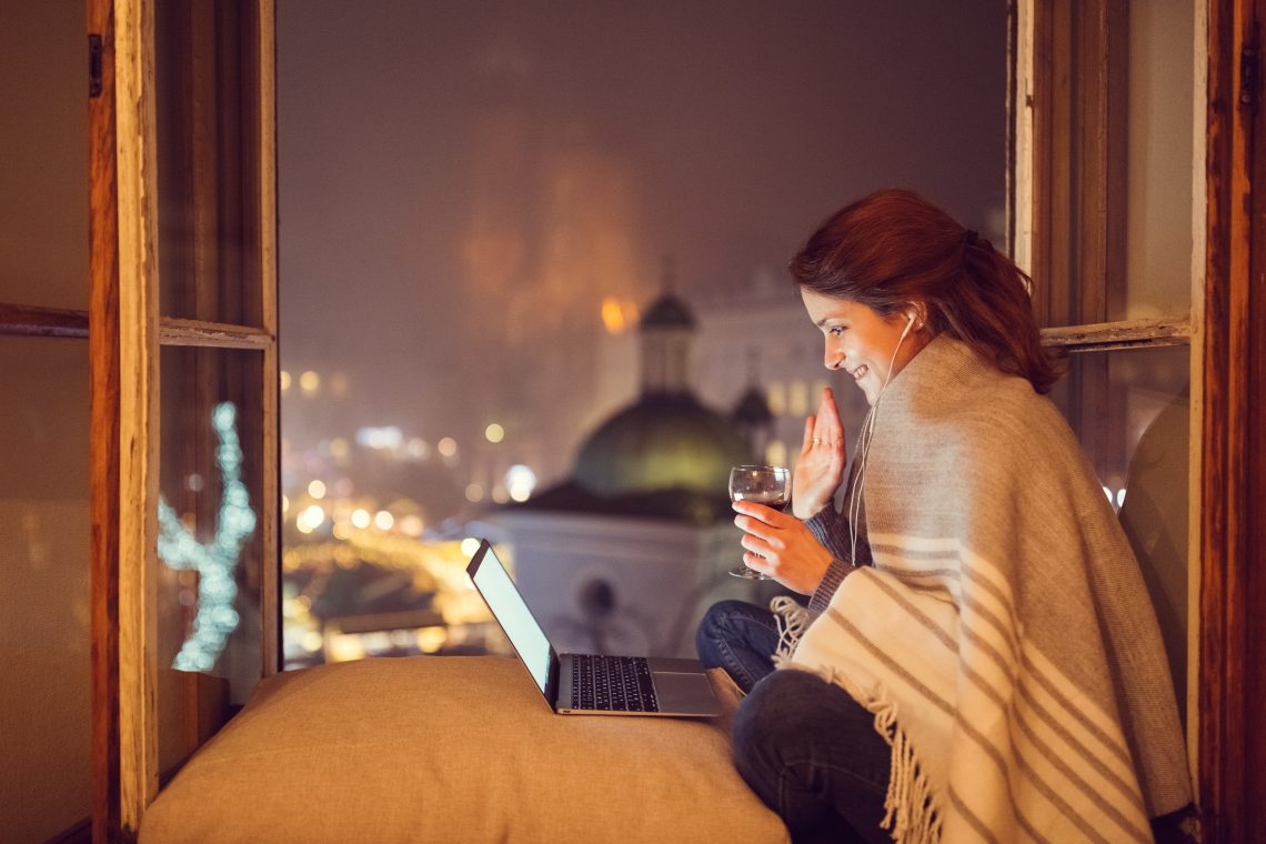 dziewczyna siedząca przy otwartm oknie, przed nią stoi laptop, okrywa się kocem