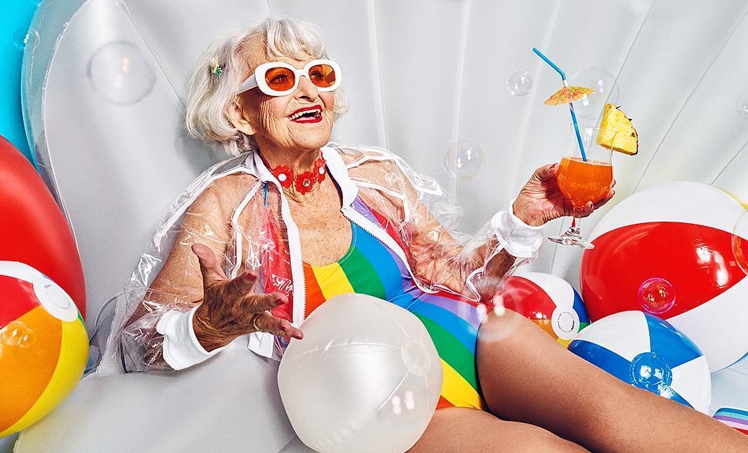 Tekst o aktywnych seniorkach inspirujących na Instagramie. Na zdjęciu: Starsza kobieta w kostiumie kąpielowym i okularach przeciwsłonecznych trzymająca napój - HelloZdrowie