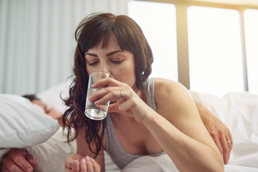 kobieta leży w łóżku i pije wodę ze szklanki