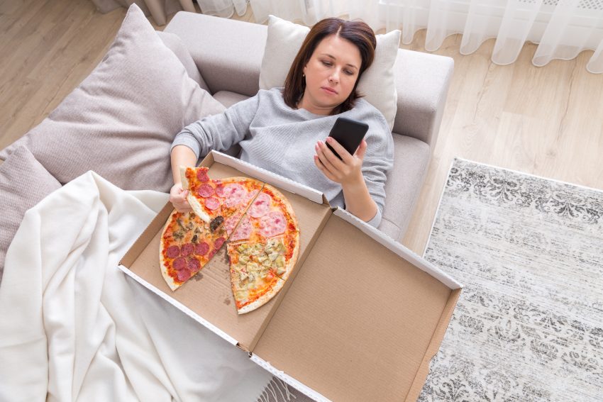 Kobieta leży na łózku i je pizze