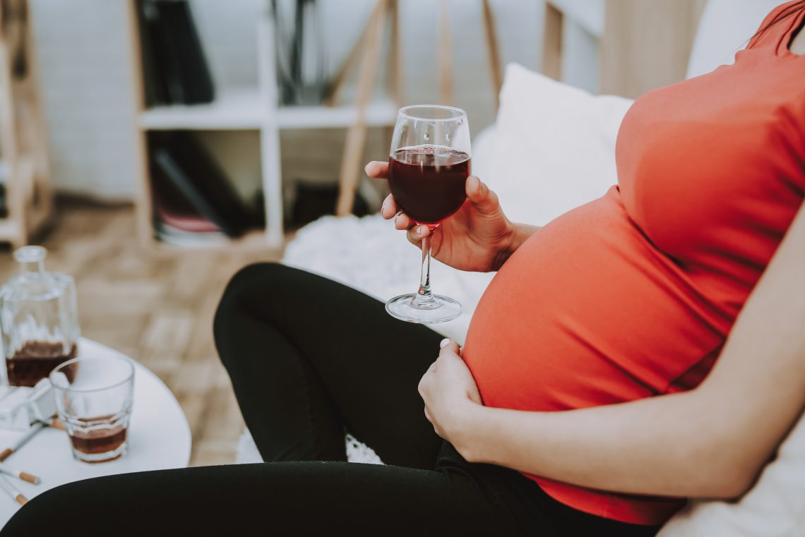 Tekst o skutkach picia alkoholu w ciąży. Na zdjęciu: Kobieta w ciąży trzymająca kieliszek wina - HelloZdrowie