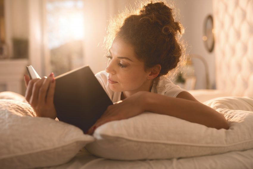 kobieta leży na łóżku i czyta książkę