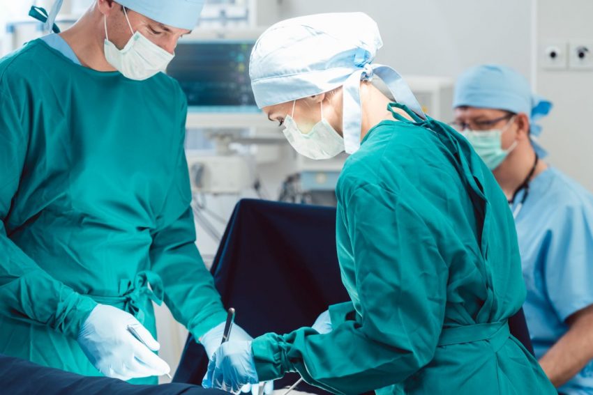 Trzech lekarzy w zielonych fartuchach operuje na sali operacyjnej.
