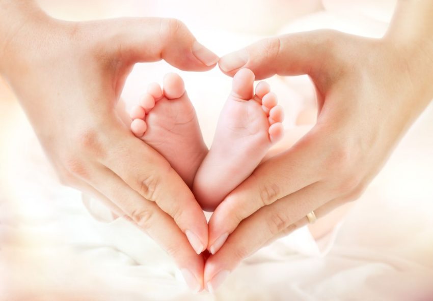 Rodzic układa serce z dłoni, w nim są stopy dziecka