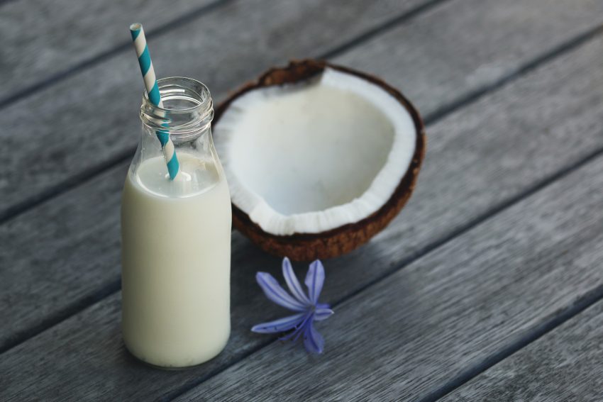 Tekst o domowej produkcji mleka roślinnego. Na zdjęciu: Butelka mleka obok kokosa - HelloZdrowie