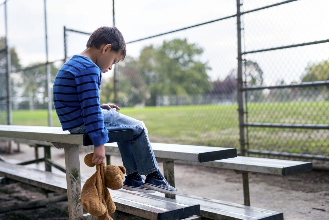 Tekst o niewydolności psychiatrii dziecięcej w Polsce. Na zdjęciu: Chłopiec siedzący na trybunach trzymający pluszowego misia - HelloZdrowie