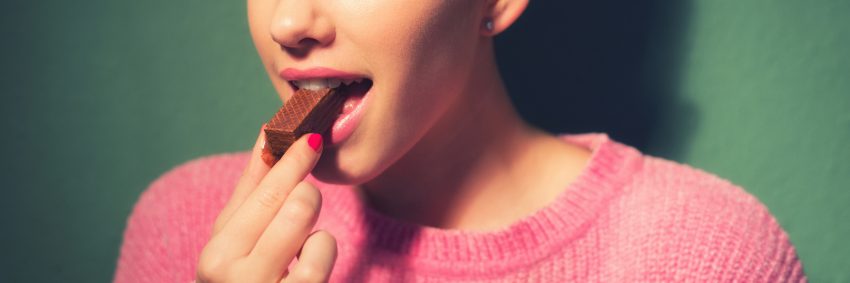 Tekst o nadmiernym spożyciu cukru i otyłości Polaków. Na zdjęciu: Kobieta jedząca batonik czekoladowy - HelloZdrowie