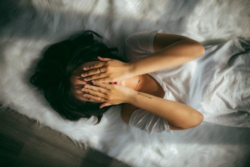 Kobieta leży na łóżku i zakrywa twarz dłońmi