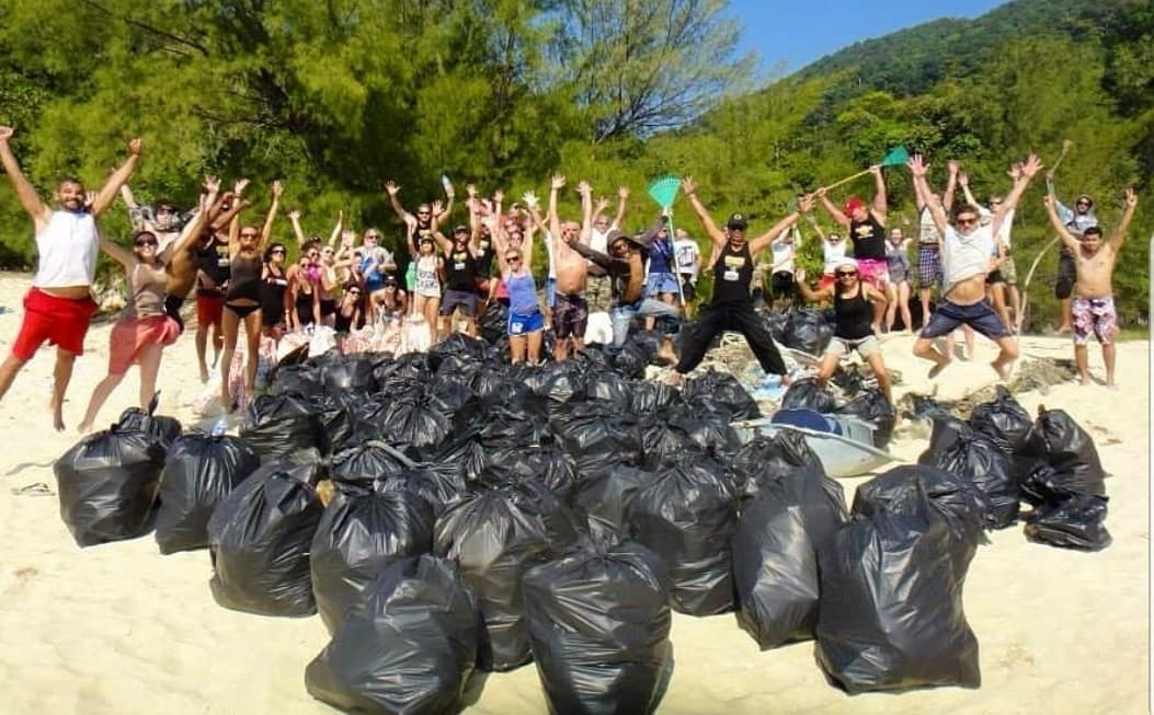 Tekst o globalnej akcji sprzątania w mediach społecznościowych. Na zdjęciu: Grupa osób stojąca na stosie worków na śmieci - HelloZdrowie