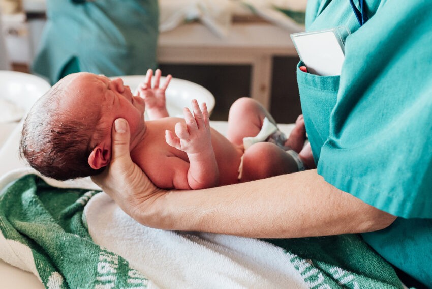 Neonatolog, czyli lekarz specjalista opiekujący się noworodkami; na zdjęciu lekarz trzymający noworodka- Hello Zdrowie