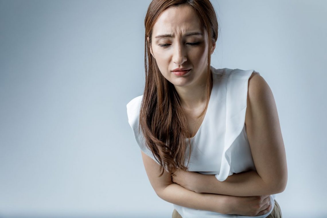Kobieta w białej bluzce trzyma się z bólu za brzuch