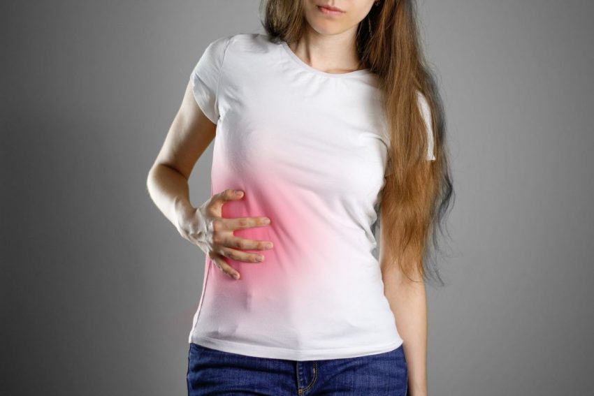 Kobieta w białej bluzce trzyma się za brzuch w okolicy wątroby