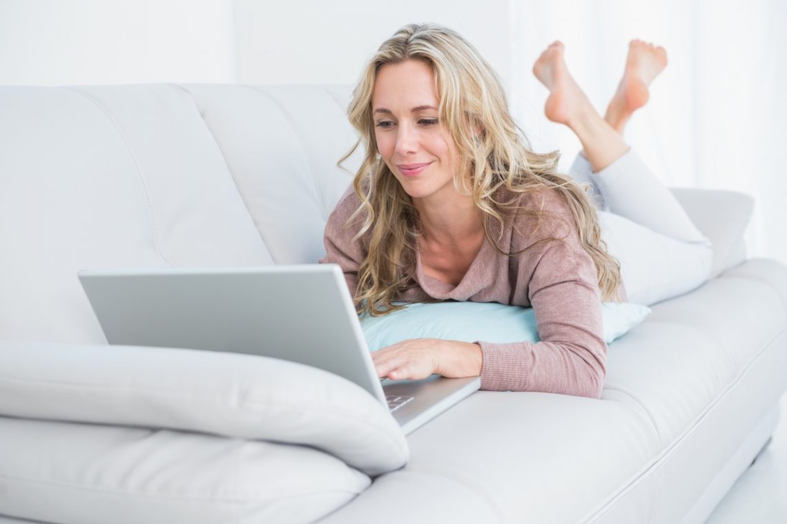 Hipokinezja - Kobieta leżąca na kanapie z laptopem.