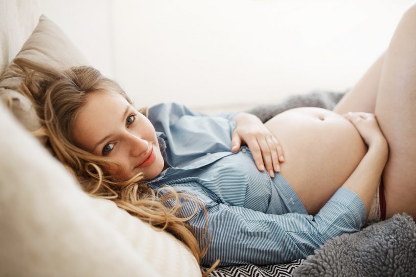 Jak przyspieszyć poród - Kobieta w zaawansowanej ciąży leży trzymając się za brzuch.