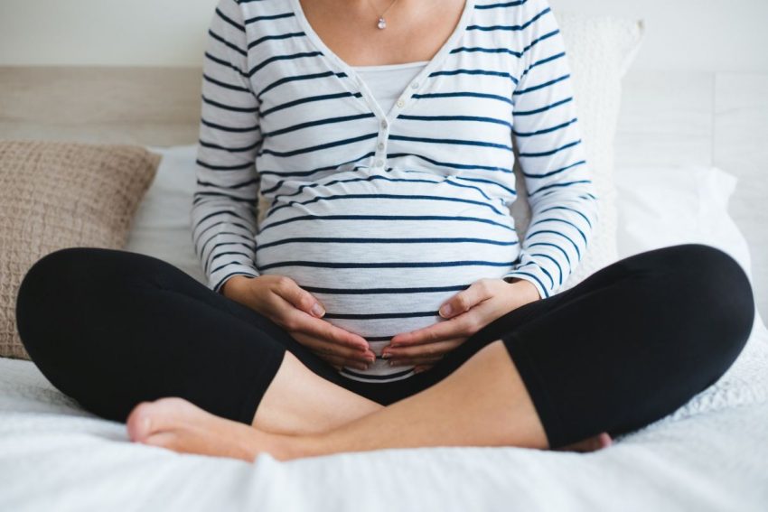 Kobieta w zaawansowanej ciąży w bluzce w paski siedzi na kanapie
